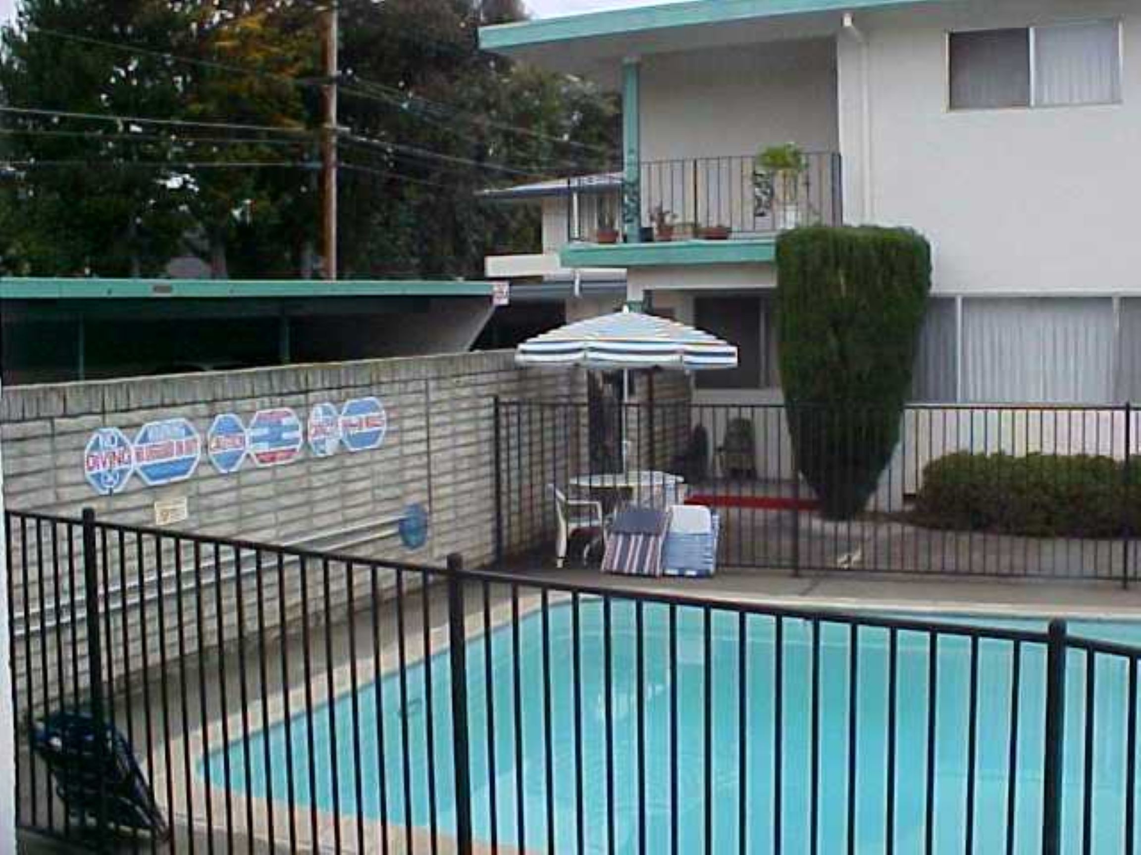 A pool with an umbrella and chairs in the back yard.